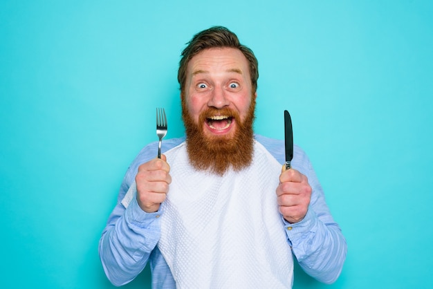 Glücklicher Mann mit Tattoos ist bereit, mit Besteck in der Hand zu essen