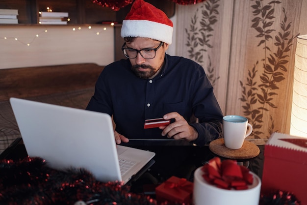 Glücklicher Mann mit Weihnachtsmann-Hut, der ein Geschenk oder eine Kreditkarte hält