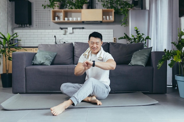 Glücklicher Mann ruht sich nach dem Morgentraining aus Asiat macht Fitness zu Hause auf einer Sportmatte