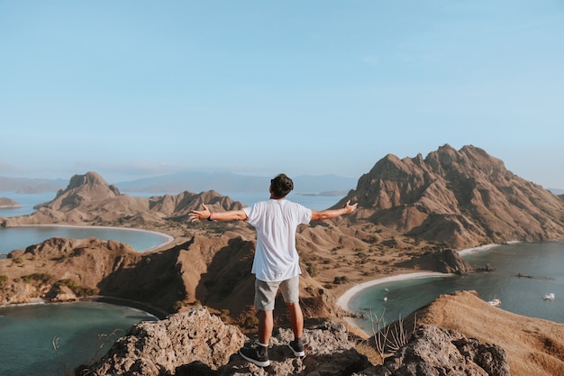 Glücklicher Mann Tourist, der auf der Spitze des Felsenberges steht, während er den Meerblick genießt?