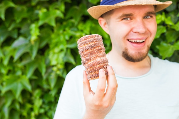 Glücklicher Mann Tourist hält in der Hand Trdlo oder Trdelnik Hintergrund. Frischer appetitlicher Trdlo oder Trdelnik - traditioneller nationaler tschechischer süßer Gebäckteig.