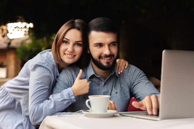 Glücklicher mann und frau, die von zu hause aus arbeiten, junges paar mit tasse kaffee, der auf laptop drinnen arbeitet