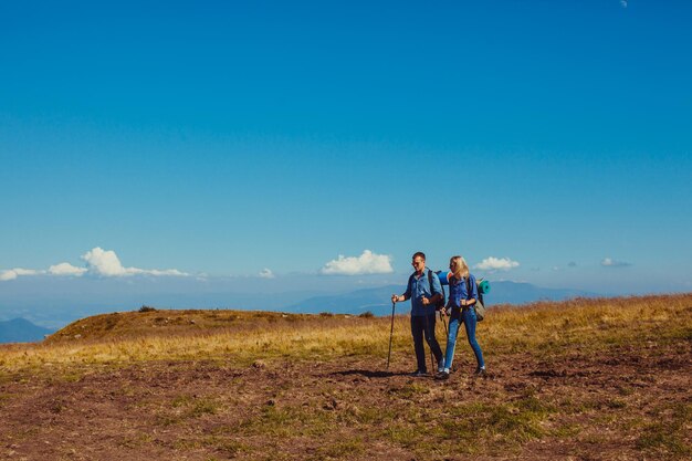 Glücklicher Mann und Frau in den Bergen. Menschen reisen mit Wanderstöcken und Rucksäcken