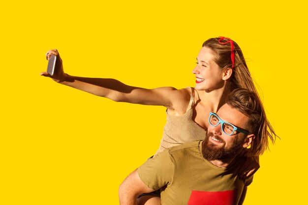 Glücklicher Mann und Frau machen Selfie auf dem Handy und haben gemeinsam Spaß beim Date Huckepack