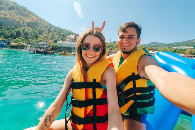 Glücklicher Mann und Mädchen machen ein Selfie, das auf einem Bananenboot auf dem Meer reitet