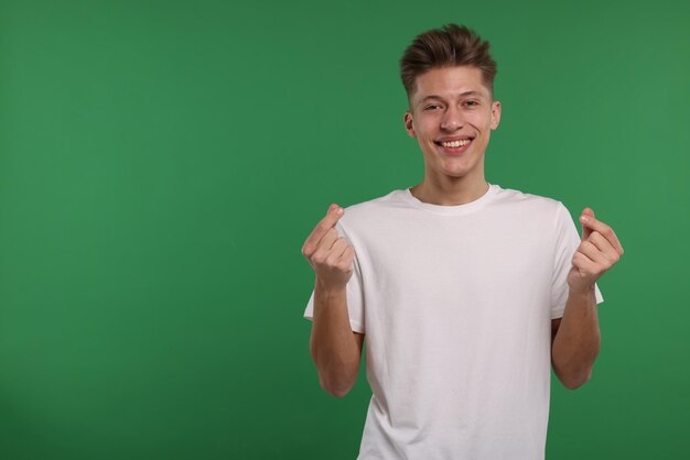 Glücklicher Mann zeigt Geldgest auf grünem Hintergrund Platz für Text