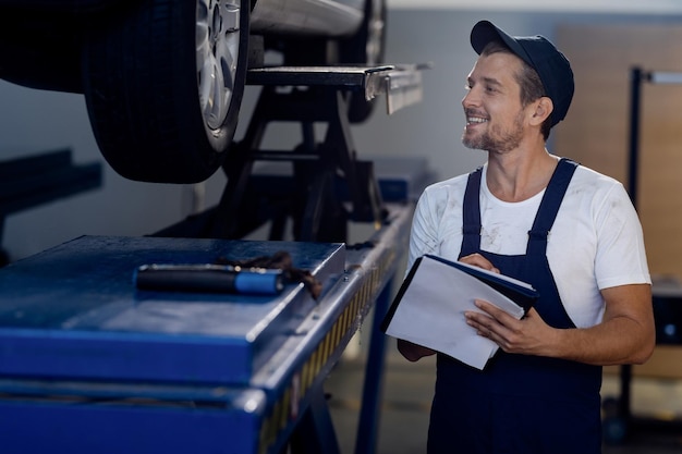 Glücklicher Mechaniker, der sich Notizen macht, während er das Auto in der Autowerkstatt untersucht