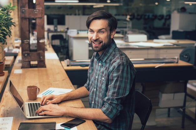 Glücklicher Mitarbeiter des Verlags, der mit den Händen auf der Laptoptastatur am Tisch sitzt und lächelt