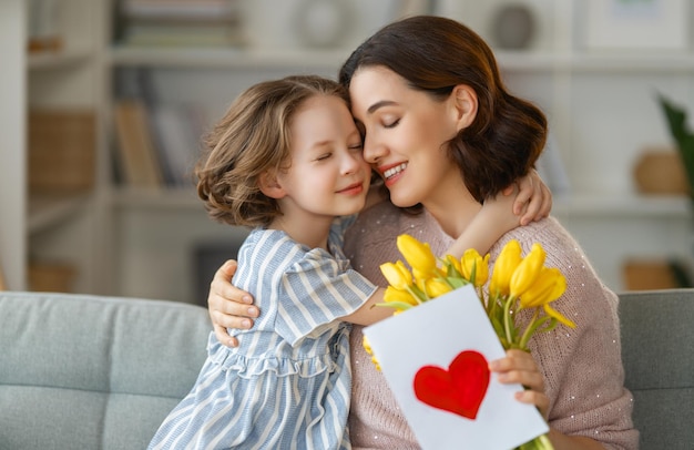 Glücklicher Muttertag Kind Tochter gratuliert Mutter und gibt ihr Blumen und Postkarte