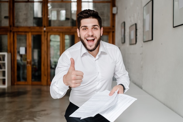 Glücklicher nahöstlicher Büroangestellter, der Daumen lächelt und sich zeigt