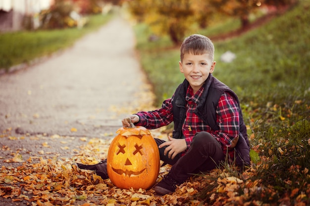 Glücklicher netter Kleinkindjunge mit Halloween-Kürbis im Herbstpark.