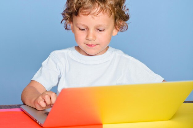 Glücklicher netter kluger Jungeschüler mit Laptop. Kind aus der Grundschule. Fröhliches lächelndes Kind benutzen Laptop-Computer. Fröhlicher lächelnder kleiner Schüler, der Spaß mit Notebook hat.