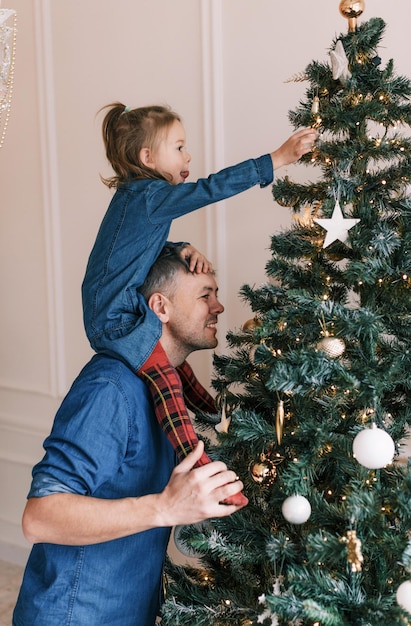 Glücklicher Papa und Tochter schmücken den Weihnachtsbaum Ein kleines Mädchen sitzt auf Papas Schultern