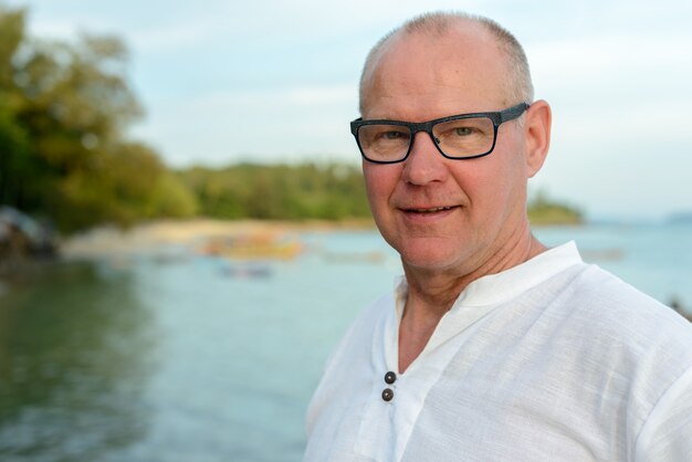 Glücklicher reifer hübscher Touristenmann, der gegen Ansicht des Strandes draußen lächelt