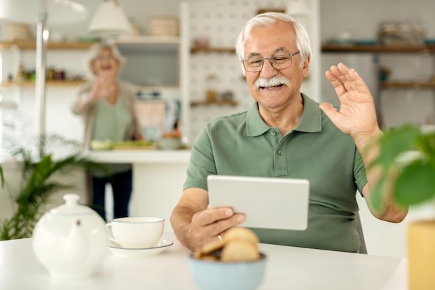 Glücklicher reifer Mann, der einen Videoanruf über das Touchpad hat und jemandem zuwinkt