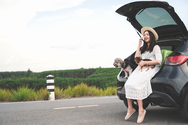 Foto glücklicher reisender der jungen frau, der im auto mit hunden auf straßen- und sonnenunterganghimmel sitzt.