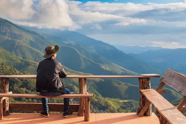 Glücklicher reisender Mann, der szenische Landschaftsansicht oben auf Berg sitzt und schaut