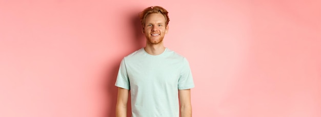 Glücklicher rothaariger Mann im T-Shirt, der in die Kamera blickt und über rosa Hintergrund lächelt