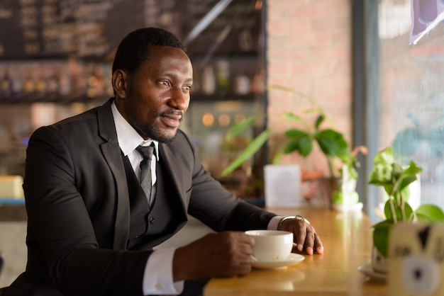 Glücklicher schöner bärtiger afrikanischer Geschäftsmann, der am Kaffeehaus denkt