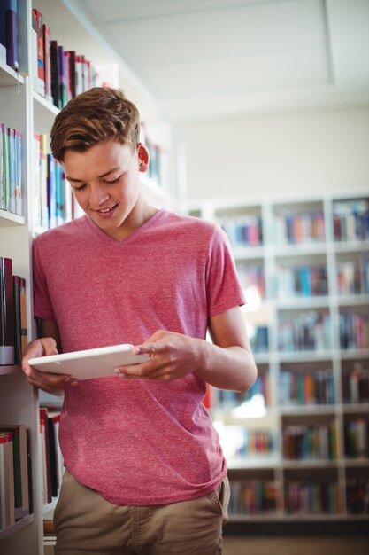 Glücklicher Schüler, der digitales Tablett in Bibliothek verwendet