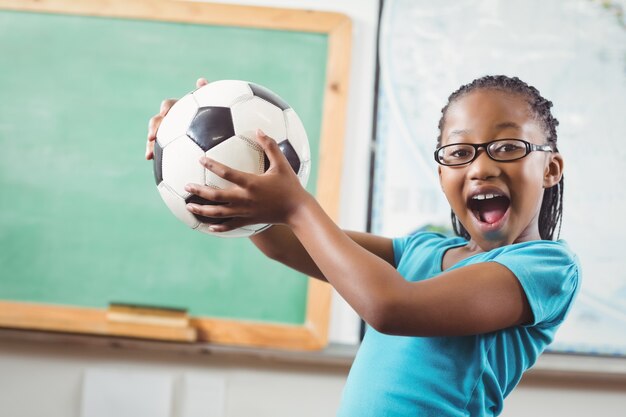 Glücklicher Schüler, der Fußball in einem Klassenzimmer hält