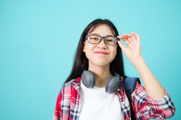 Glücklicher Schüler. Fröhliches asiatisches Mädchen, das zur Kamera lächelt, die mit Rucksack im Studio über blauem Hintergrund steht. Zurück zum Schulkonzept.