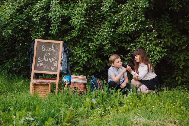 Foto glücklicher schüler und schulmädchen untersuchen die blumen unter einer lupe