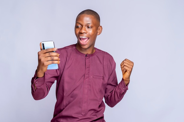 Glücklicher schwarzer Kerl im authentischen afrikanischen Kostüm unter Verwendung des weißen Hintergrundkopienraumes des Handys