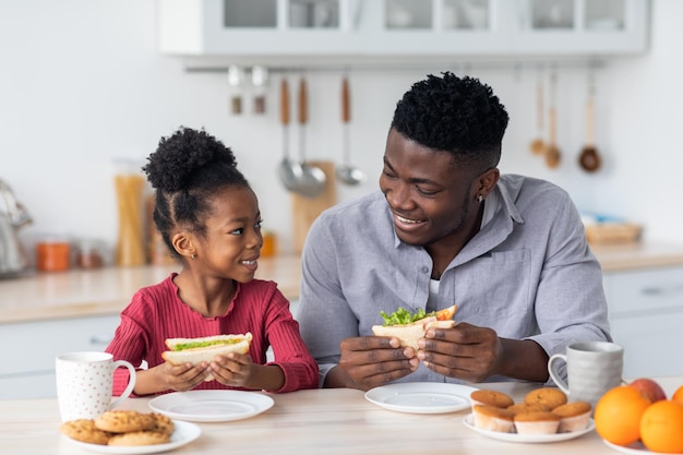 Glücklicher schwarzer Vater und Kind, die zu Hause einen Snack essen