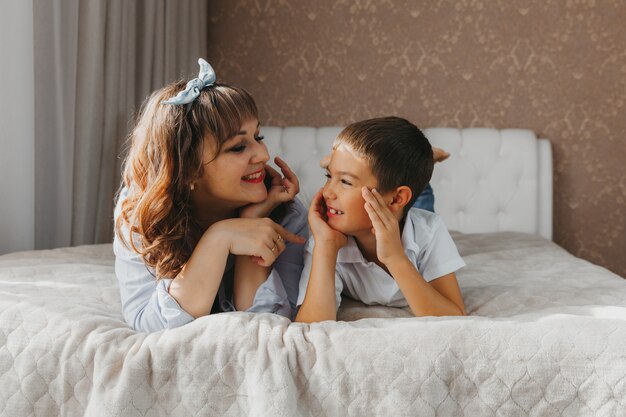 Glücklicher Sohn und Mutter liegen auf dem Bett und lachen. Muttertag!