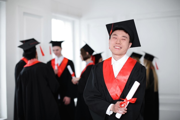 Glücklicher Student in Junggesellenrobe mit Diplom drinnen Graduierungstag