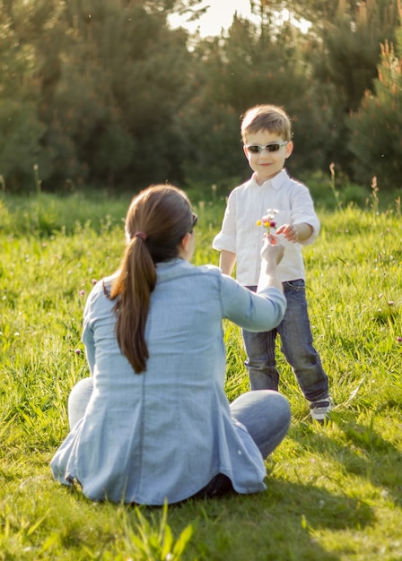 Glücklicher süßer Sohn, der seiner Mutter auf einem sonnigen Feld einen Blumenstrauß schenkt