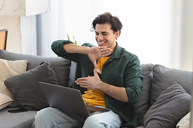 Glücklicher tauber junger kaukasischer Mann verwendet Gebärdensprache während Videoanrufe mit Laptop, während er zu Hause auf der Couch sitzt