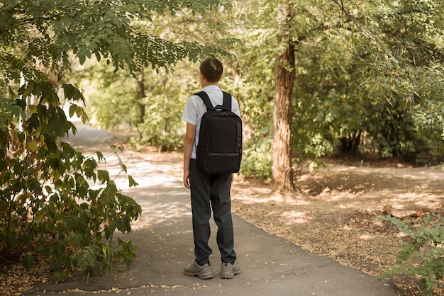 Glücklicher Teenager steht im Herbst mit einer Aktentasche auf den Schultern auf der Straße. Bald wieder in der Schule.