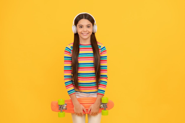 Glücklicher Teenie-Mädchen-Skateboarder hört Musik in Kopfhörern mit Penny-Board-Skateboard-Kindheit