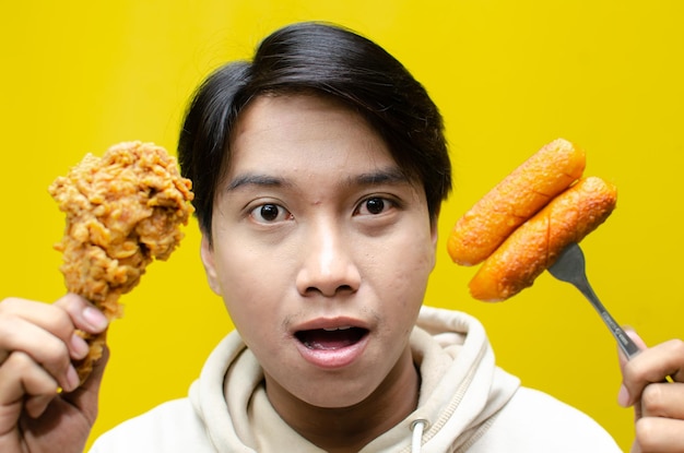 Glücklicher überraschter asiatischer Mann hält gebratenes Huhn und Würstchen mit Wow-Ausdruck isoliert