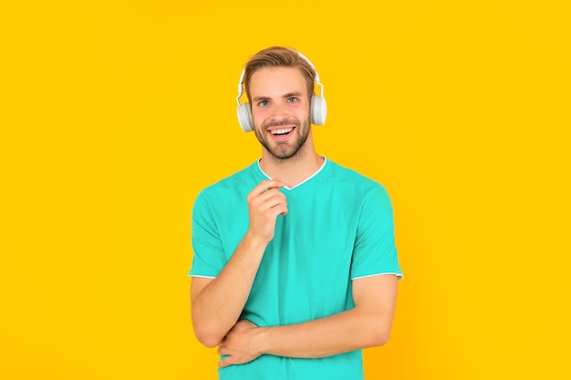 Glücklicher unrasierter junger Mann mit Kopfhörern auf gelbem Hintergrund, Musik