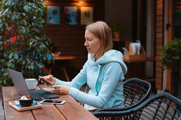 Glücklicher Unternehmer, der mit einem Telefon und einem Laptop in einem Café auf der Straße arbeitet