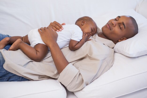 Glücklicher Vater, der mit Babysohn auf Couch Nickerchen macht