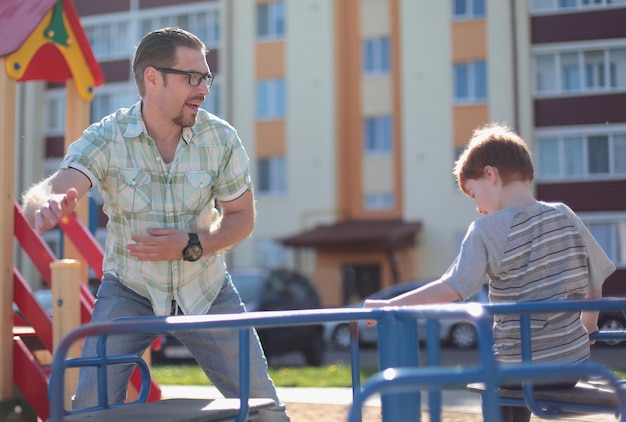 Glücklicher Vater, der mit kleinem Jungen auf dem Spielplatz spielt, das Konzept der Elternschaft