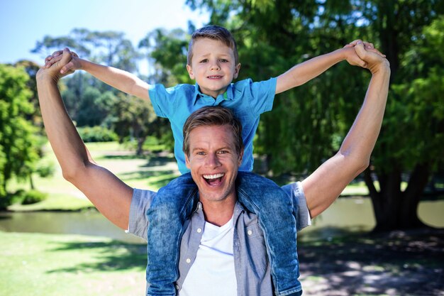 Foto glücklicher vater, der seinen sohn auf der schulter im park trägt