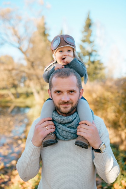 Glücklicher Vater, der seinen Sohn auf Schultern im Herbstpark hält