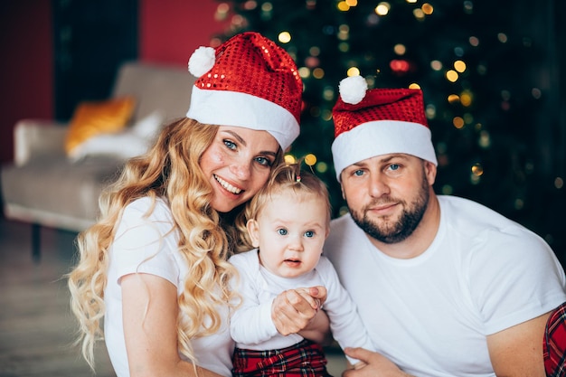 Glücklicher Vater in Weihnachtsmütze in der Nähe seiner Frau und seines Babys zu Hause