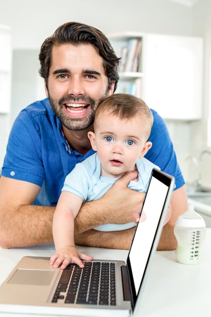 Glücklicher Vater mit dem Sohn, der sich bei Tisch durch Laptop lehnt