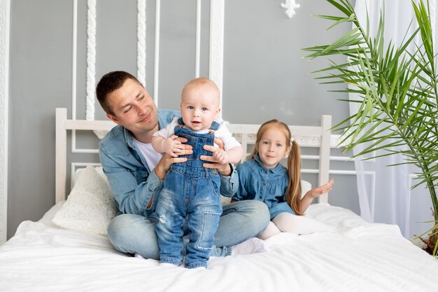 Glücklicher Vater mit Kindern Sohn und Tochter kuscheln auf dem Bett zu Hause Vatertagskonzept