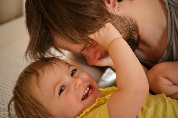 Glücklicher Vater mit Tochter, kleines Mädchen, einjähriges Baby, lächelnd, lachend, mit Blick auf Daddy Man, der Zuneigung zum Kind zeigt, offen, echte Emotionen, Bart, Vater und kleines Kind, authentischer Familienlebensstil