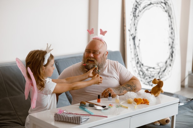 Glücklicher Vater spielt Schönheitssalon mit kleinem Mädchen, das zu Hause einen Feenanzug trägt