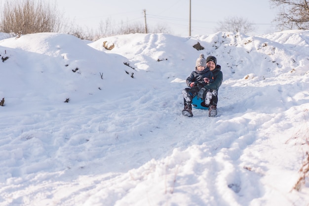 Glücklicher Vater und kleiner Junge spielen mit Schneeschlitten