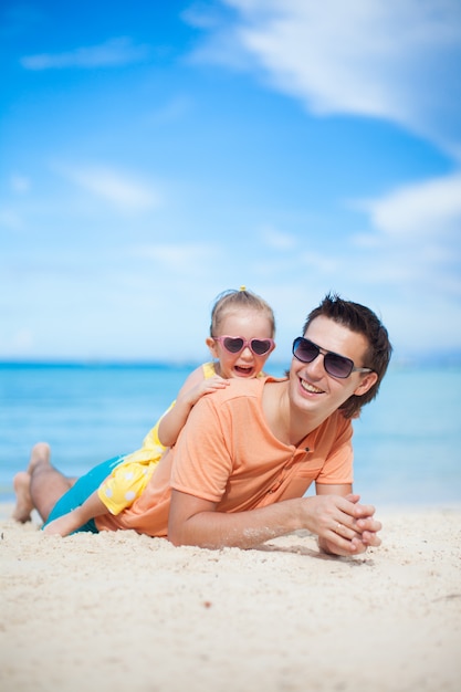 Glücklicher Vater und seine entzückende kleine Tochter, die auf weißem Sandstrand liegt