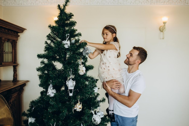 Glücklicher Vater und seine kleine Tochter schmücken den Weihnachtsbaum zu Hause